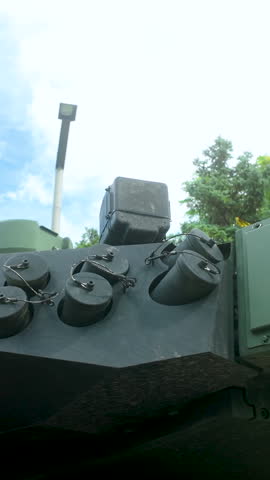 A detailed lowangle shot of a modern armored vehicle turret featuring smoke grenade launchers and reactive armor plates against a blue sky.