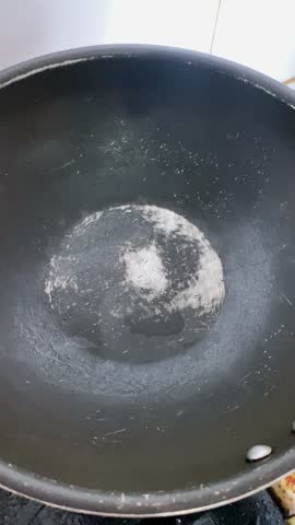 A video of oil being poured into a hot, black pan.