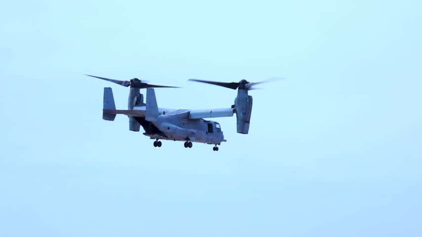 US Military V-22 Osprey Tiltrotor Aircraft Hovering In Blue Sky During Routine Tactical Mission.