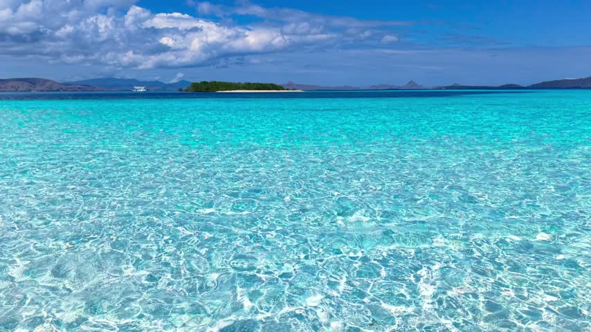 Aerial view of clear turquoise sea with coral reef, a small sandbar island, and a boat at Taka Makassar Island, Komodo, Flores, Indonesia.