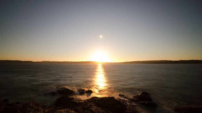 A locked-off timelapse captures sunset fading over Luderitz Bay, Namibia. Warm amber light gives way to twilight above the rocky Atlantic coastline.