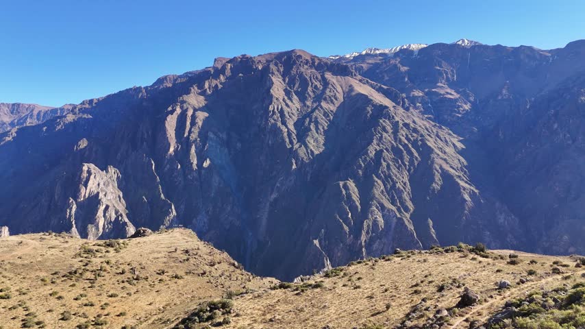 Aerial view rising slowly above the vast Colca Canyon in Peru, revealing rugged mountains, deep valleys, and distant snow-capped peaks.