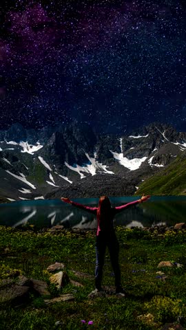 Milky Way Galaxy glowing over a scenic alpine lake and snowy peaks with a traveler raising hands