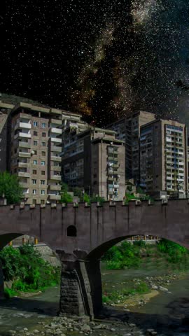 Milky Way Galaxy rising above urban apartment buildings and an old bridge across the river. Kapan city in Armenia