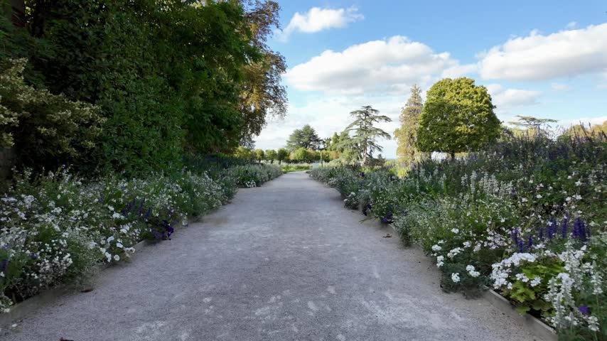 Walking path approaching Château de Chaumont-sur-Loire through landscaped gardens with hedges, flowers and mature trees