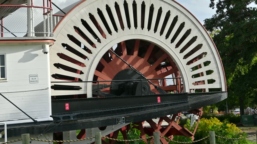 Static shot of a large historic waterwheel next to a white building under natural daylight in Penticton, British Columbia.