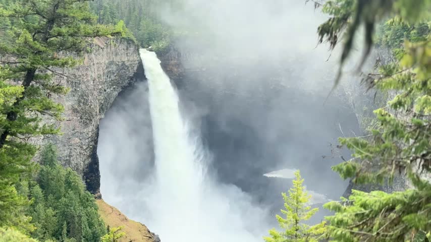 Static shot of Helmcken Falls framed by evergreens as it plunges into a misty canyon at Wells Gray Provincial Park near Clearwater, British Columbia.