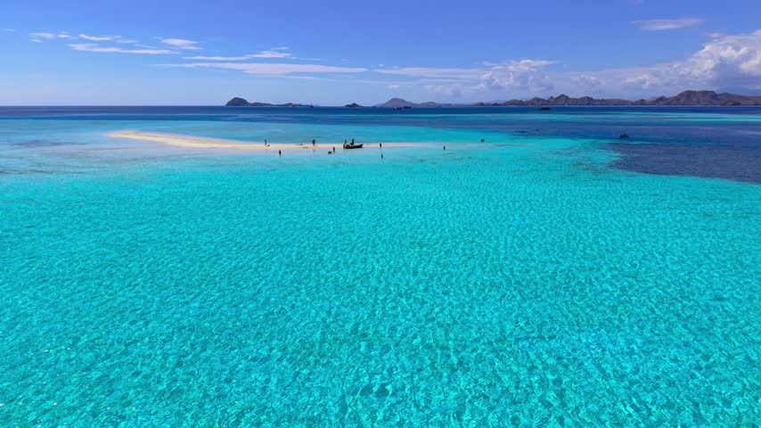 Aerial view of men and women walking on a white sandbar surrounded by turquoise ocean water at Taka Makassar island, Komodo, Flores, Indonesia.