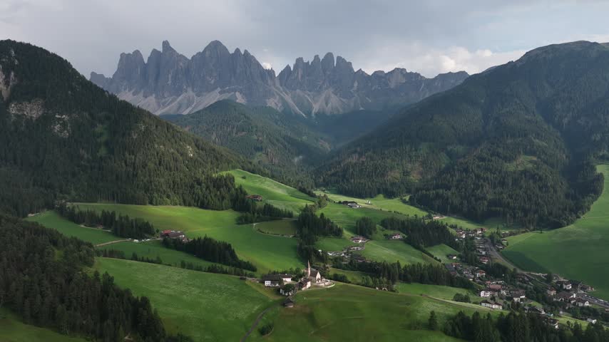 serene rural valley with mountains in the background, aerial perspective of grassy meadows and rocky terrain, houses nestled among nature, peaceful landscape for travel and nature scenes.