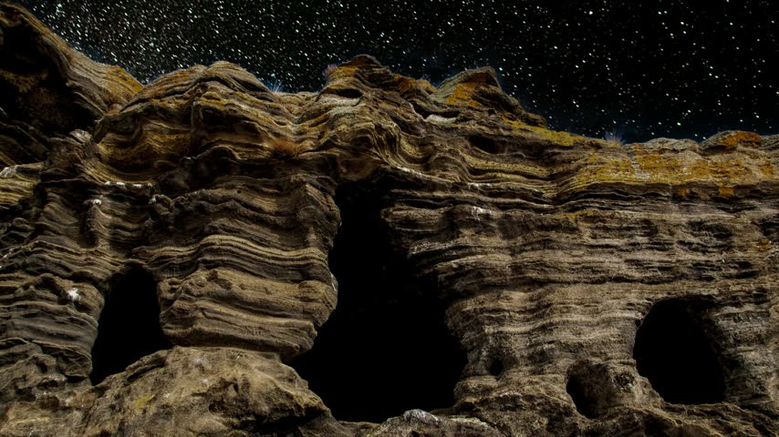 Milky Way Galaxy twinkling above ancient carved rock dwellings and caves in a canyon cliff