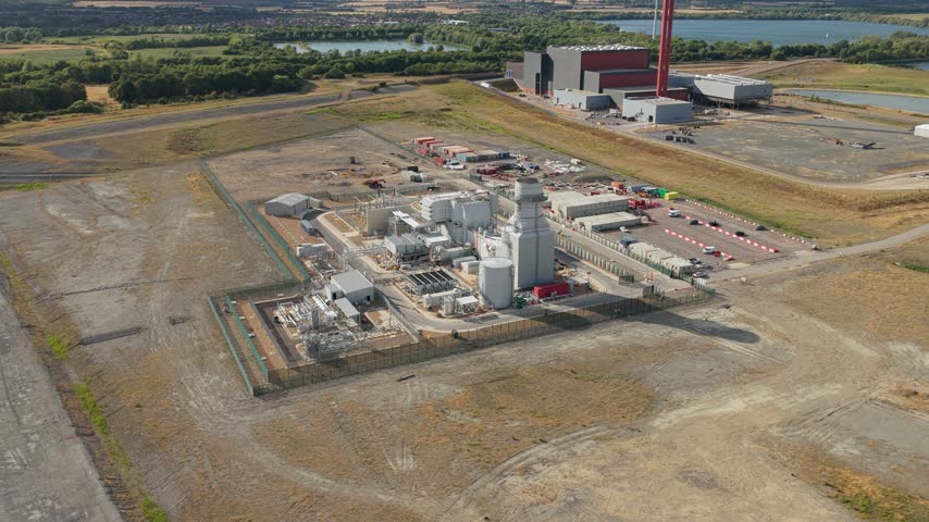 A waste-to-energy facility stands amid rural fields and water, generating sustainable power on a sunny day.