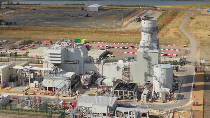 Large facility generates electricity from waste materials using industrial machinery and tall chimneys located in an open area during bright daylight conditions