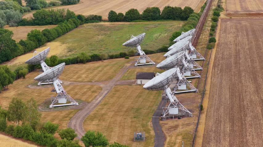 Large white satellite dishes line a rural field, collecting radio waves from space as birds fly over the scientific facility.