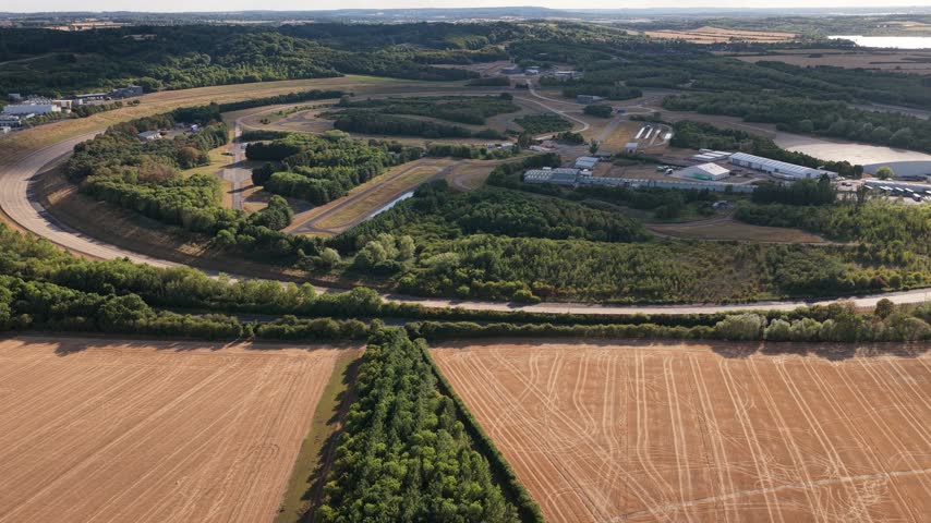 High angle perspective of a professional vehicle testing facility located in a rural landscape during the day with various tracks and buildings visible among trees and dry agricultural fields