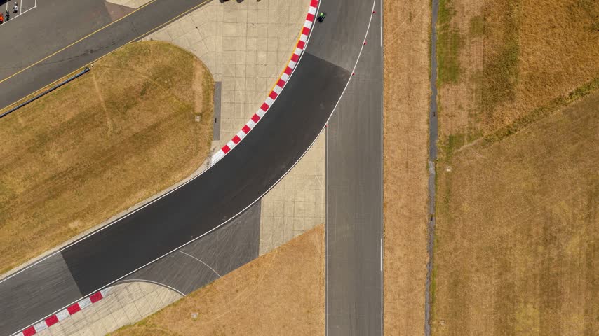 Black race car speeding around a red and white curve on a sunny day at a professional circuit facility in Europe during a bright afternoon competition