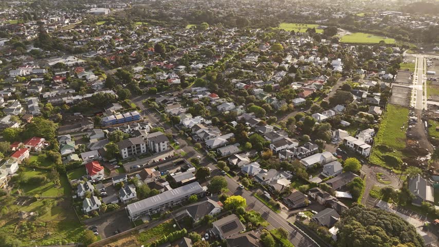 Drone view flying over grid of residential houses and streets with green trees in Mount Albert suburb of Auckland, New Zealand