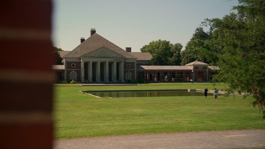 Scenic view of the historic Hall of Springs in Saratoga Springs, New York, framed by lush green lawns, a tranquil reflecting pool, and mature shade trees.