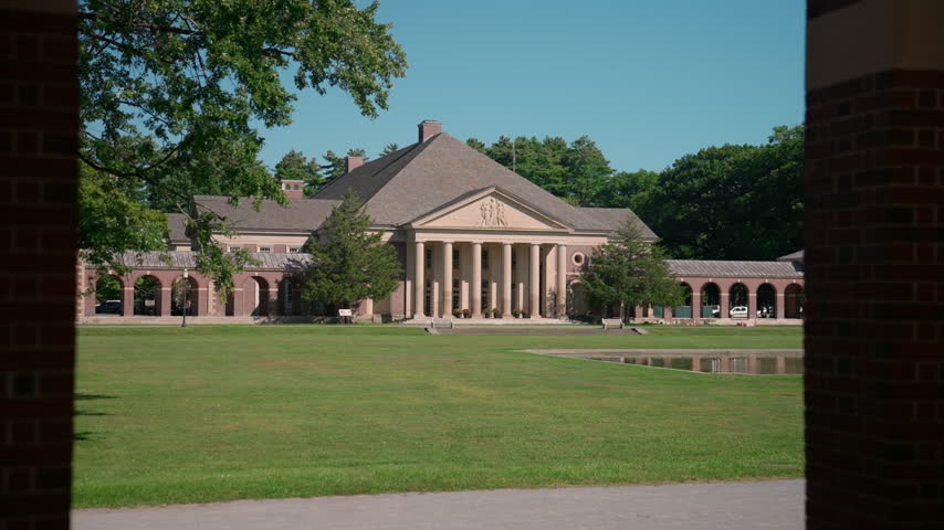 Scenic view of the historic Hall of Springs building in Saratoga Springs, New York, with its grand columned facade, arched brick walkways, and lush green lawn.