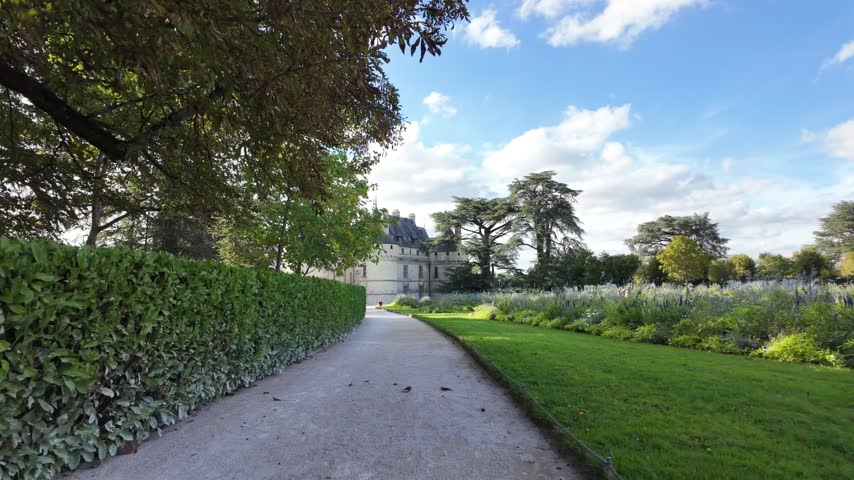 Walking path approaching Château de Chaumont-sur-Loire through landscaped gardens with hedges, flowers and mature trees
