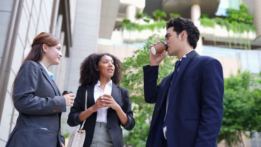 Morning stand-up outdoors: a businessman finishes a call and turns to his two colleagues, who listen with coffee cups in hand, then all three laugh in a green garden courtyard.