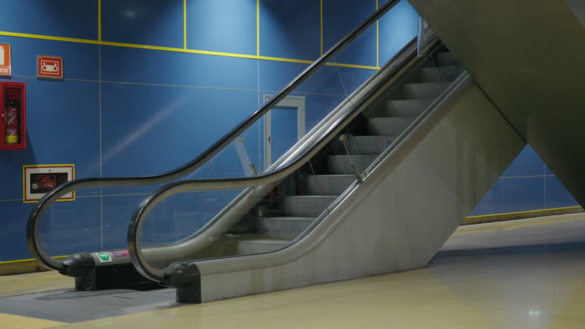Rear view of a young woman walking and riding up an escalator in a modern subway station.