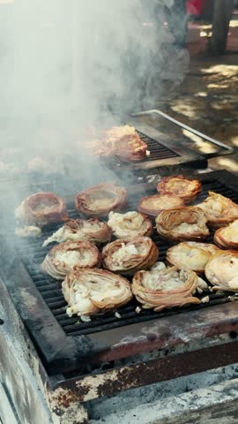 Vertical video of rolled meat slices grilling on outdoor grill with smoke. Barbecue cooking process, street food preparation on charcoal grill. High quality 4k footage