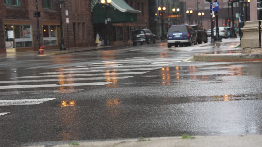 Video frame of various cars driving on a wet asphalt street, splashing water and reflecting lights during a rainy day. Ideal for urban traffic, transportation, and weather concepts. Horizontal shot, 4K resolution.