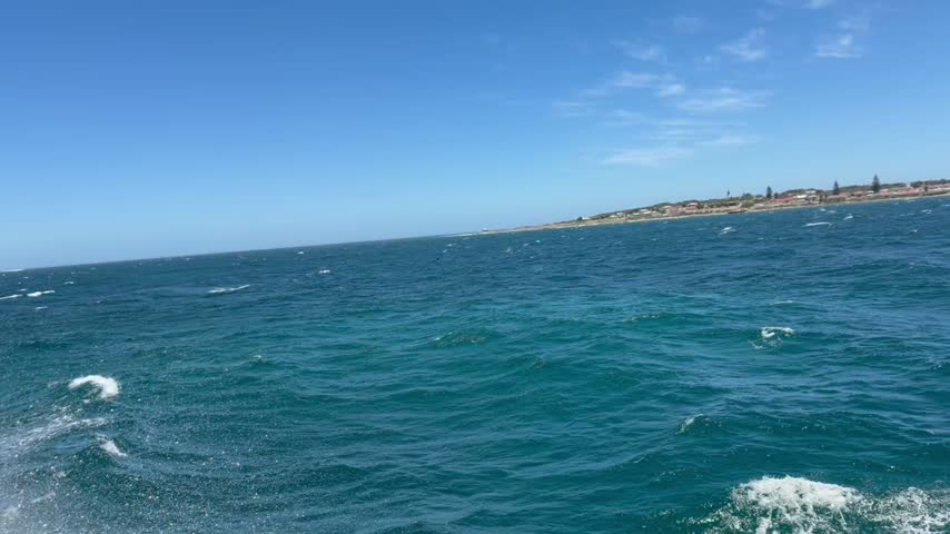Boat wake across choppy Table Bay with the low shoreline of Robben Island on the horizon, Cape Town, South Africa