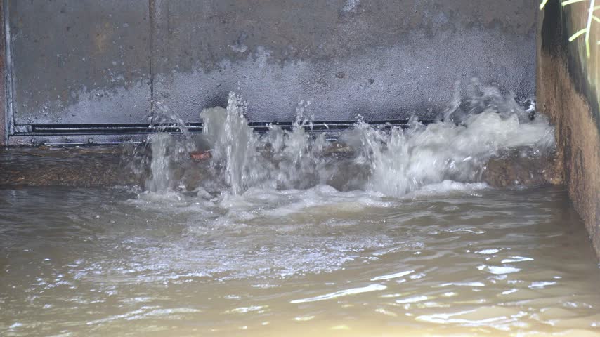 Water Releasing from Dam Sluice Gate into Irrigation Canal Close Up View. Water Splashing from Open Canal Sluice Gate in Agricultural Irrigation System.