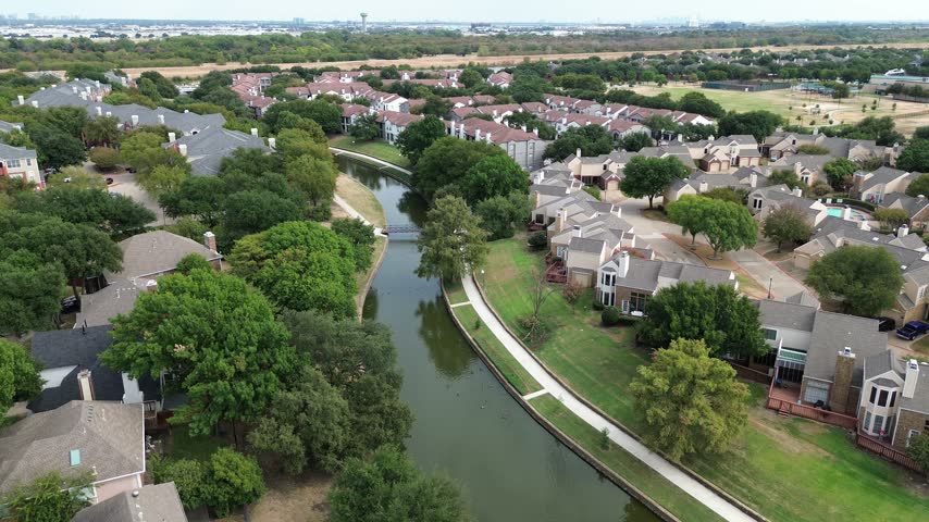 Camera tracks long waterway meandering past compact townhomes dense foliage. Peaceful suburban atmosphere prevails throughout Valley Ranch, Irving, Texas, Valley Ranch, Irving, Texas. US.