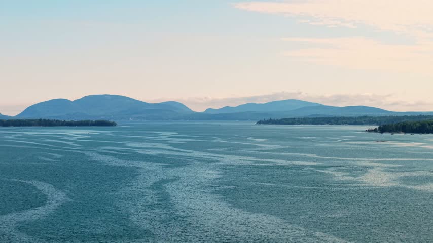 Mountain peaks of Acadia National Park rising on Mount Desert Island across the wide, swirling waters of Mount Desert Narrows, captured in a high-angle aerial photograph from Sullivan, Maine.