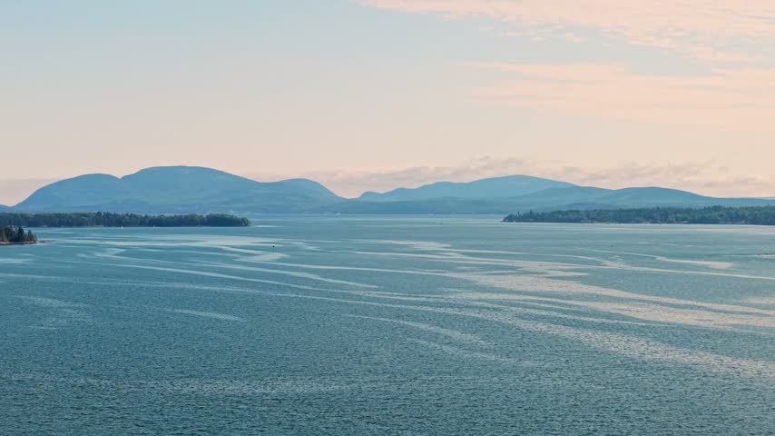 Mountain peaks of Acadia National Park rising on Mount Desert Island across the wide, swirling waters of Mount Desert Narrows, captured in a high-angle aerial photograph from Sullivan, Maine.