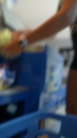 Blurred person leaning forward and reaching toward foreground under bright strip light, with cool blue kiosk display in background and diagonal arm gesture