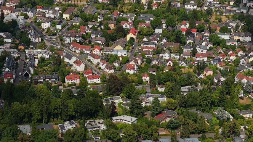 Telephoto slow pullback with gentle tilt up over residential red rooftops and green trees in sunny summer light, Bad Homburg, Hesse, Taunus, Germany