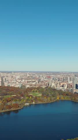 Vertical video: Idyllic autumn day. Aerial view of colourful Central Park with water reservoir and buildings in town around. Clear blue sky. Manhattan, New York City, USA