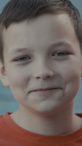 Close-up of a calm young boy in an orange shirt looking at the camera outdoors.