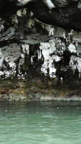 Underground limestone cave with white stalactites hanging over calm turquoise water.