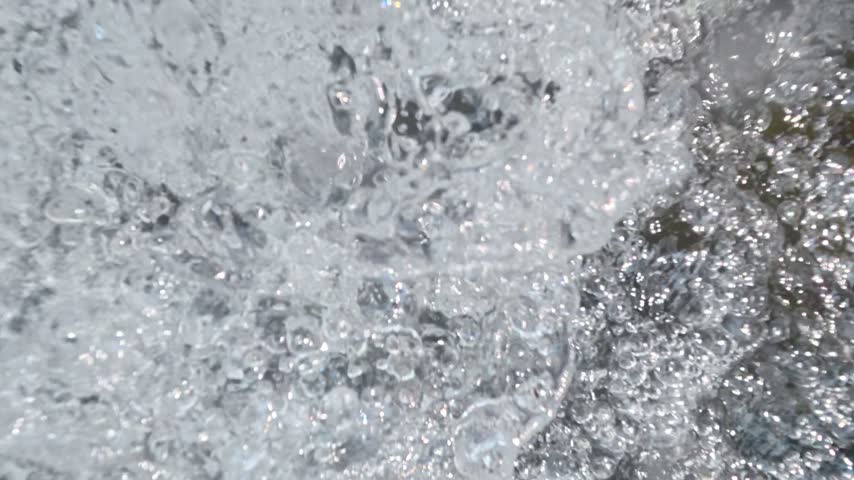 Close up cinematic footage of turbulent splashing water and white foam flowing rapidly over a rocky riverbed
