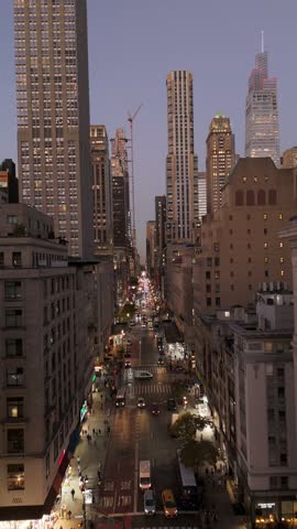 Vertical view of traffic moving on Fifth Avenue, Midtown Manhattan, New York City. Cars and taxis drive down the street with the city skyline in the background