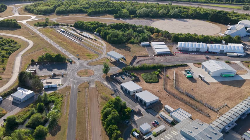 Wide view of a Vehicle Testing Facility with various testing tracks and buildings set within a large outdoor landscape during a bright sunny day of automotive research