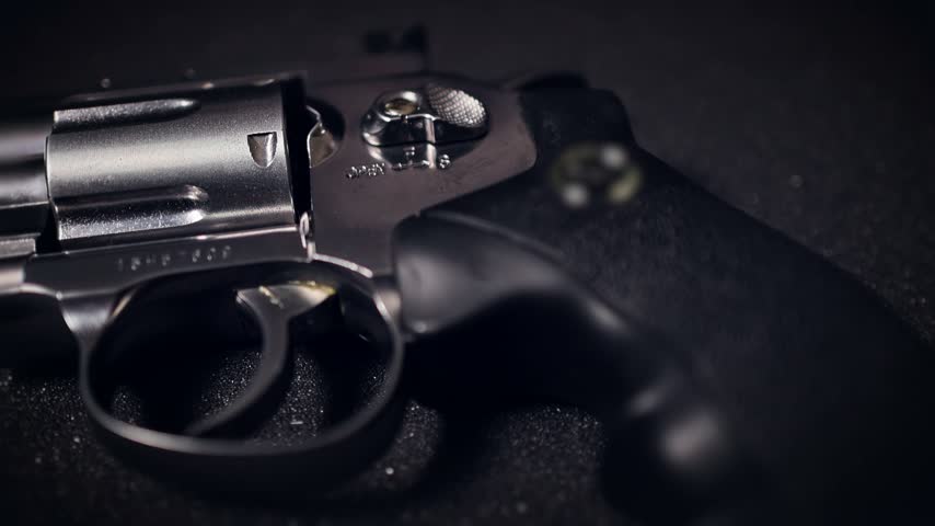 A black metal revolver handgun is shown in close up detail against a dark textured background.