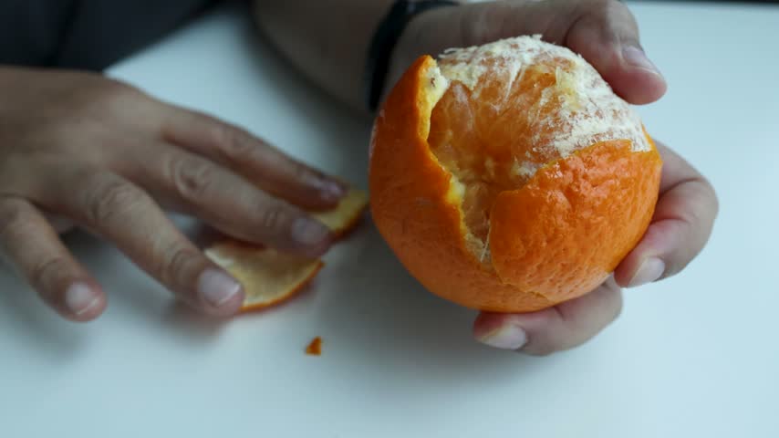 Close-up of human hands peeling a fresh juicy mandarin orange over a white surface.
