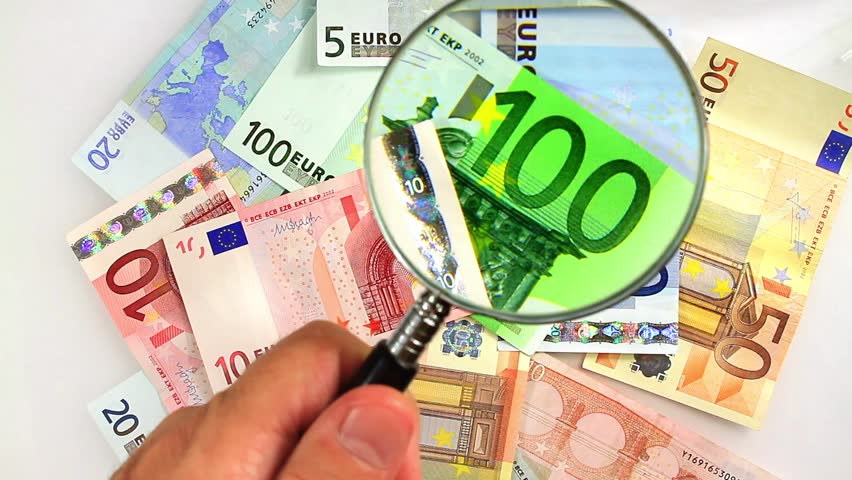 Hand holding magnifying glass up to Euro banknoes for economists.