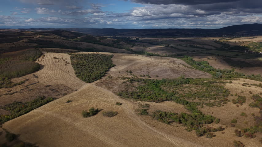 An expansive aerial view of a rugged rural landscape with dry autumn fields and patches of forest under cloudy skies.