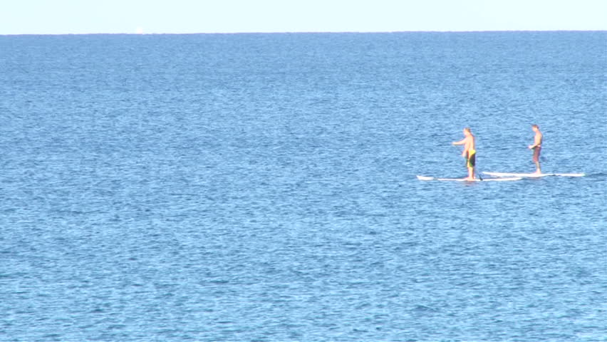 Two men paddling through frame in stand up paddle boards on calm ocean.