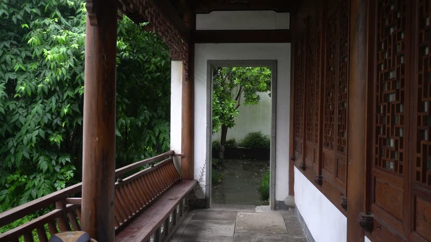 Traditional Chinese wooden pavilion corridor overlooking a lush green garden through a doorway.