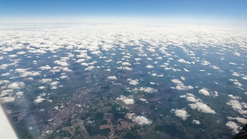 Aerial view of a town, agricultural fields and scattered clouds from high above the landscape during a flight.