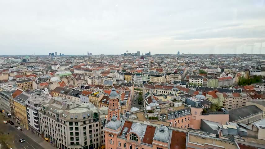 Wide aerial panorama over central Vienna, Austria, showing historic buildings, rooftops, streets and the extensive urban skyline.