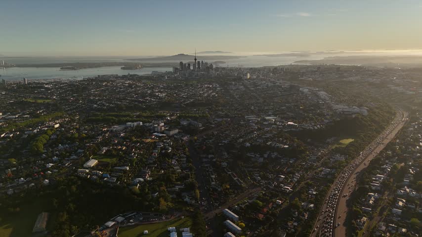 High aerial view of Auckland city skyline, Sky Tower, suburbs, and highway traffic at sunset in New Zealand