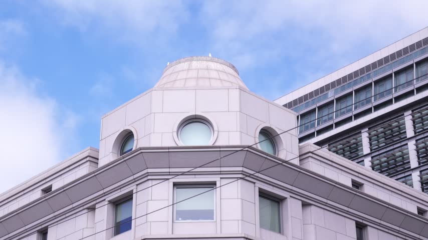 Low-angle perspective of the top corner of a historic federal government building in downtown San Francisco, California, contrasting with a modern facade under a cloudy blue sky